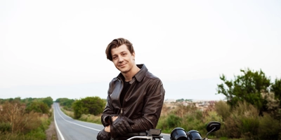 Young handsome man posing near his motorbike countryside road