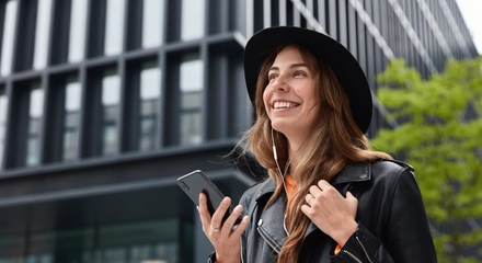 Photo charming dreamy woman holds modern cellular listens music walk outdoor metropolis