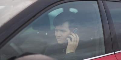 View young male wearing black jacket sitting red car while talking phone