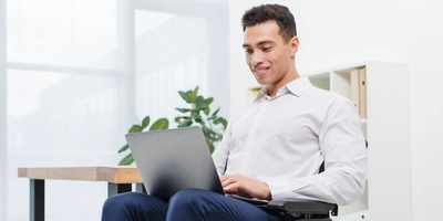 Happy disabled young businessman sitting wheelchair using laptop office