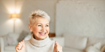 Indoor shot fashionable overjoyed mature female turtleneck sweater enjoying positive news having ecstatic facial expression laughing clenching fists success achievements concept