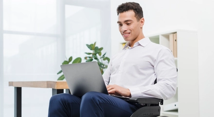 Happy disabled young businessman sitting wheelchair using laptop office