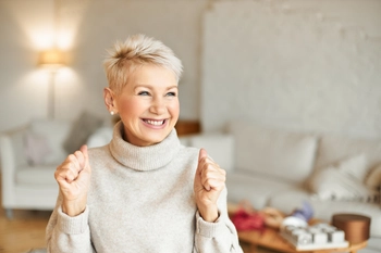 Indoor shot fashionable overjoyed mature female turtleneck sweater enjoying positive news having ecstatic facial expression laughing clenching fists success achievements concept