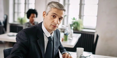 Portrait mid adult businessman sitting desk going through business reports while looking camera office