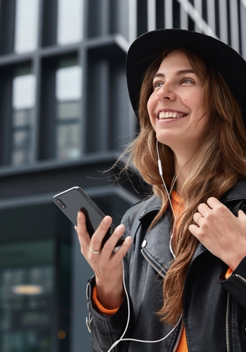 Photo charming dreamy woman holds modern cellular listens music walk outdoor metropolis