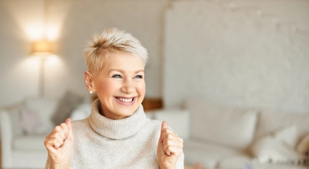 Indoor shot fashionable overjoyed mature female turtleneck sweater enjoying positive news having ecstatic facial expression laughing clenching fists success achievements concept