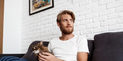 Young man smiling stroking cat sitting sofa home